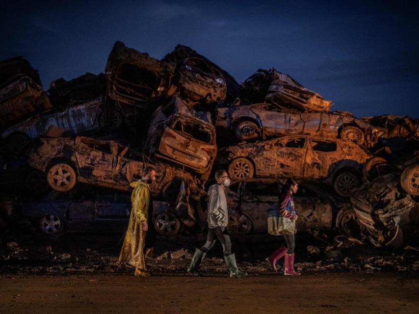 Vecinos caminan frente a decenas de coches destruidos por la riada en Paiporta, tras las inundaciones de octubre de 2024.
