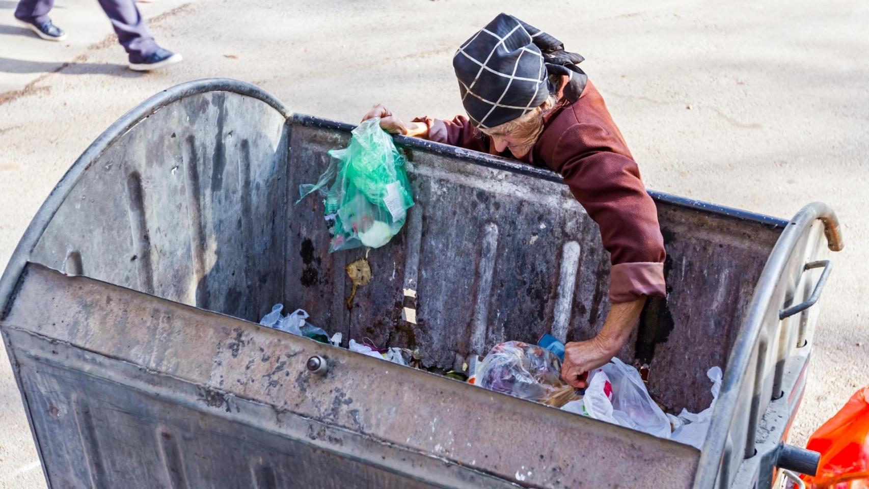 Una anciana sin recursos buscando comida en un contenedor.