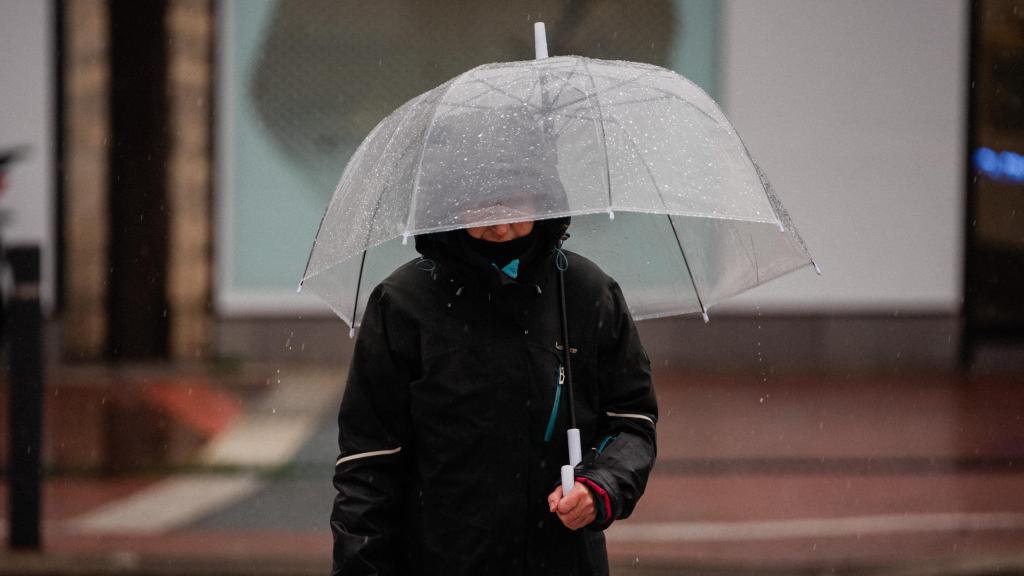 Una mujer se refugia con su paraguas de la lluvia.