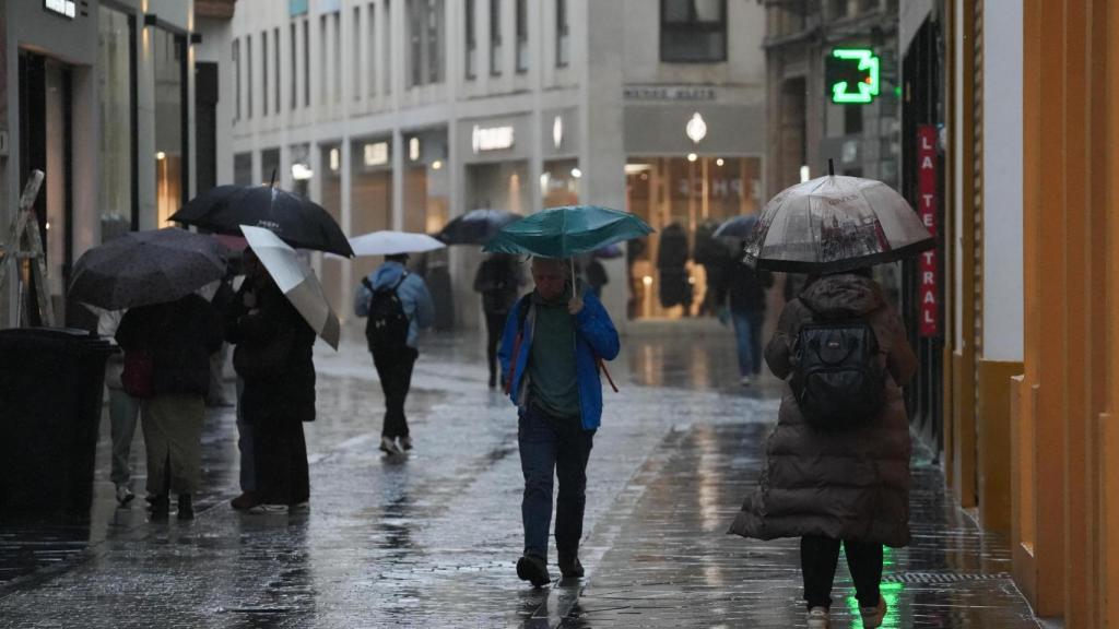 Imagen de transeúntes por el centro de la ciudad durante el temporal.