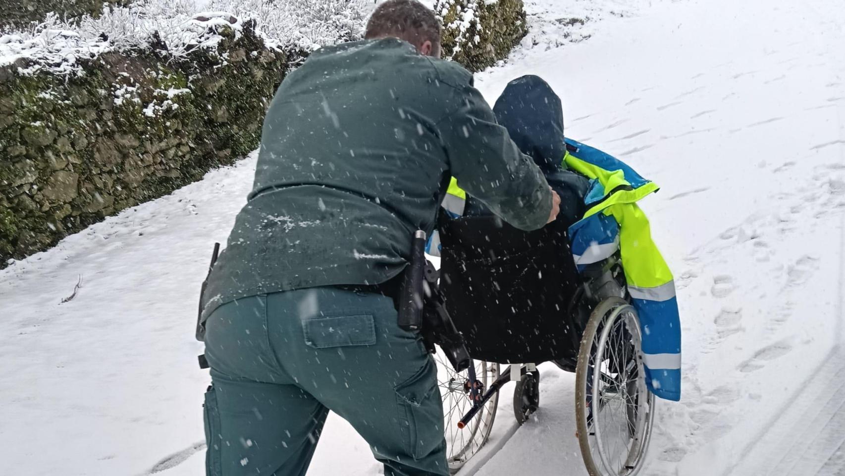 Imagen de uno de los agentes llevando al paciente en silla de ruedas tras quedar atrapada la ambulancia en la nieve en Zamora