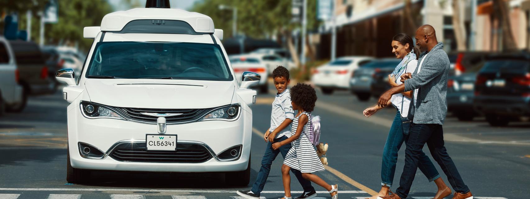 Un coche de Waymo en un paso de cebra con peatones.