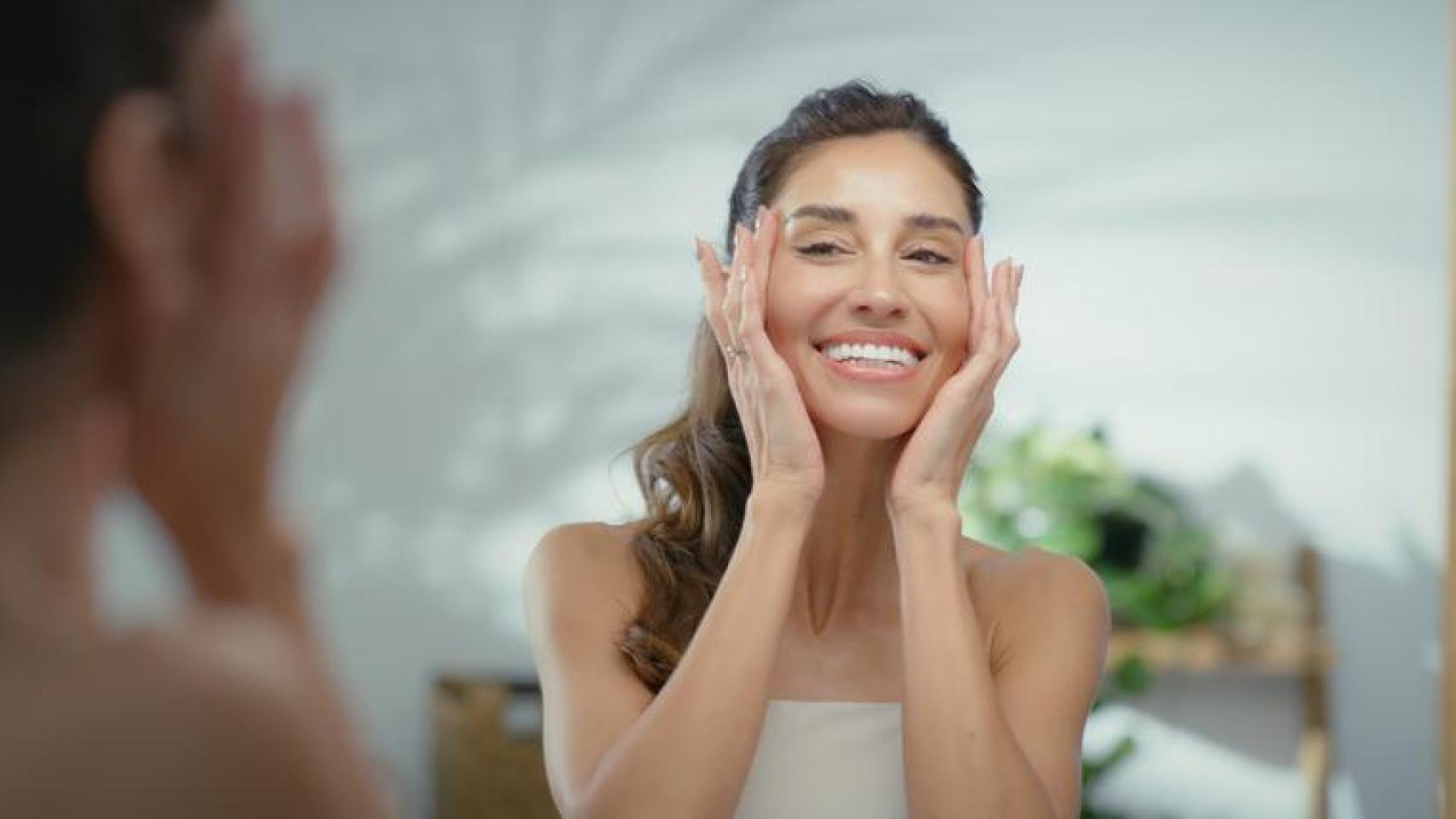 Mujer frente al espejo hidratando su piel.