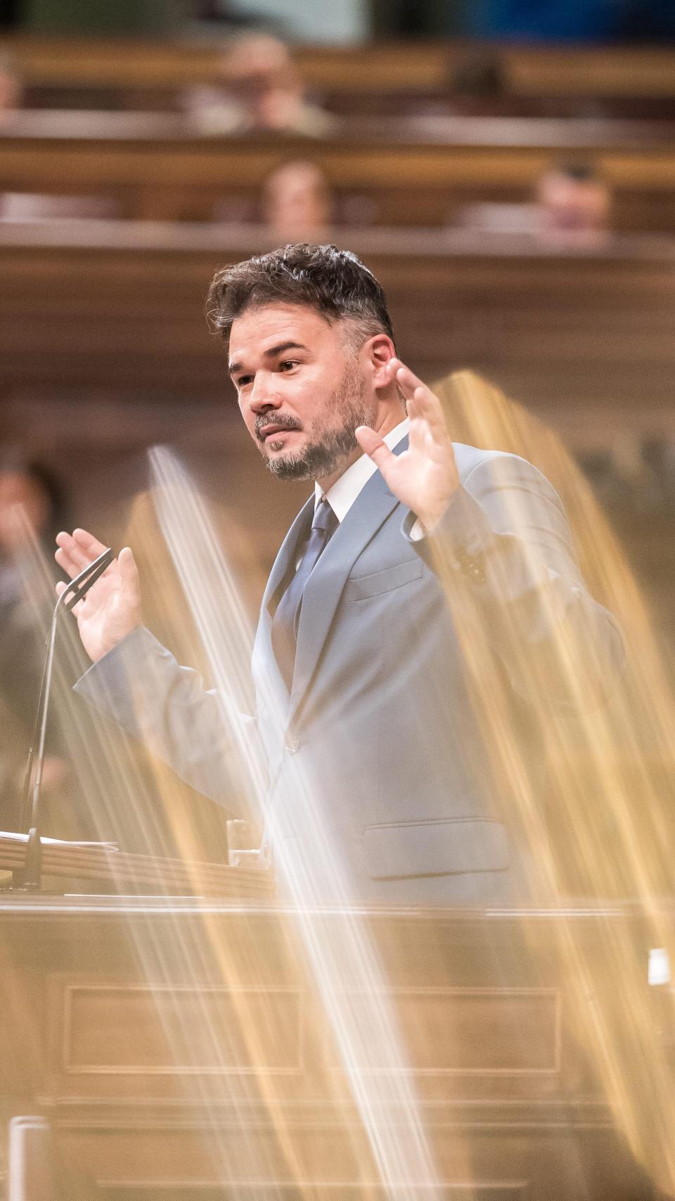 En plena intervención, Rufián abre las manos y sostiene el gesto en el aire. La luz lo corta en dos: el orador y el personaje, el foco y el ruido.