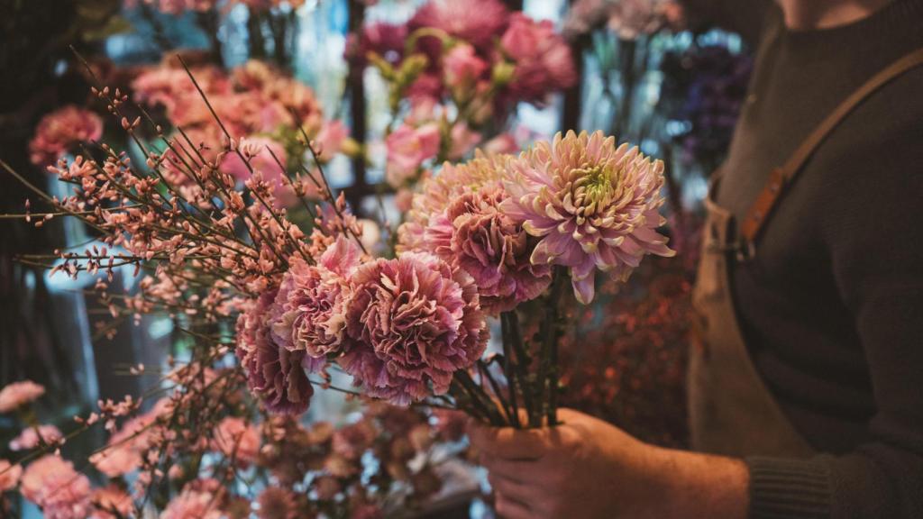 Detalle de las manos de Bonilla mientras prepara un ramo de claveles y crisantemos rosados.