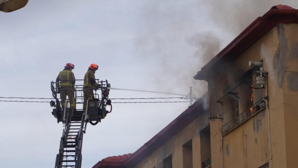 Dos bomberos echan agua a las llamas que salen del interior de una de las viviendas.