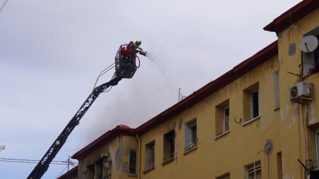 Dos bomberos tratan de apagar el fuego echando agua y espuma por el techo colapsado del edificio.