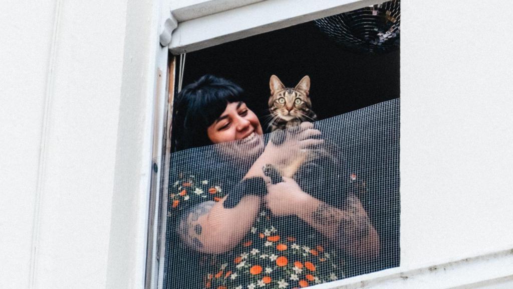 Una chica con su gato asomados a la ventana.