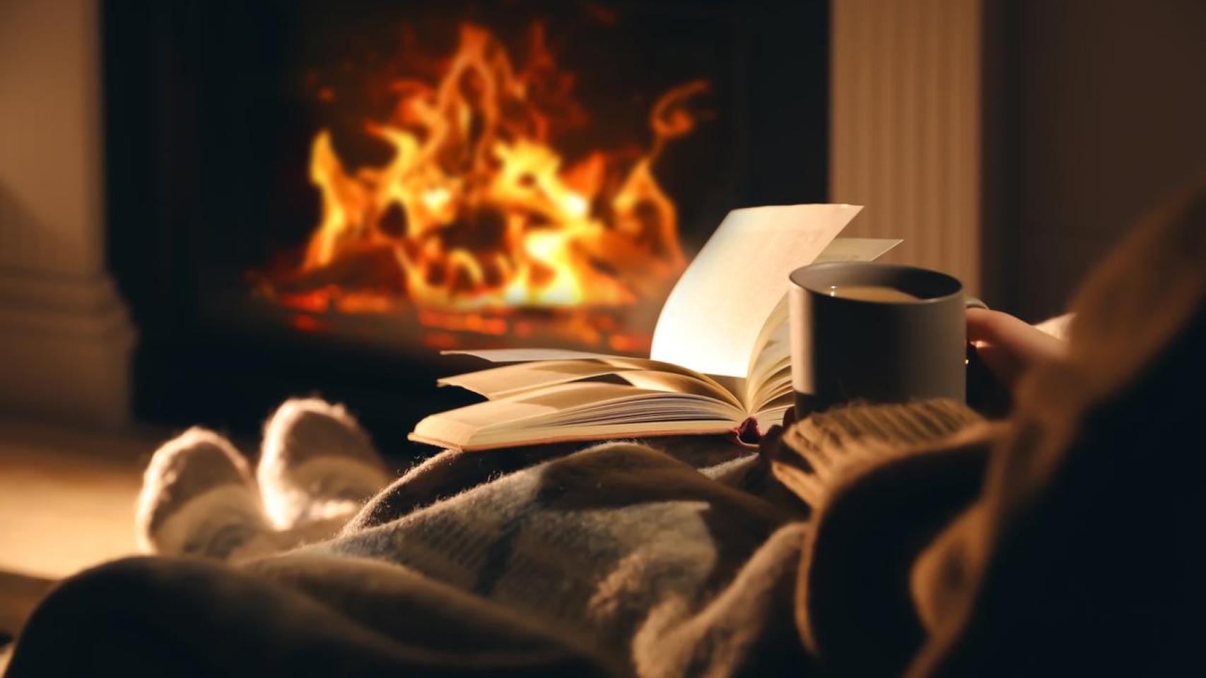 Una mujer con una taza y un libro cerca de la chimenea.