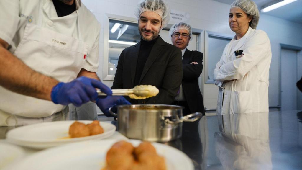 El ministro de Derechos Sociales, Consumo y Agenda 2030, Pablo Bustinduy, junto un cocinero que emplata albóndigas, durante una visita al Hospital Nacional de Parapléjicos.