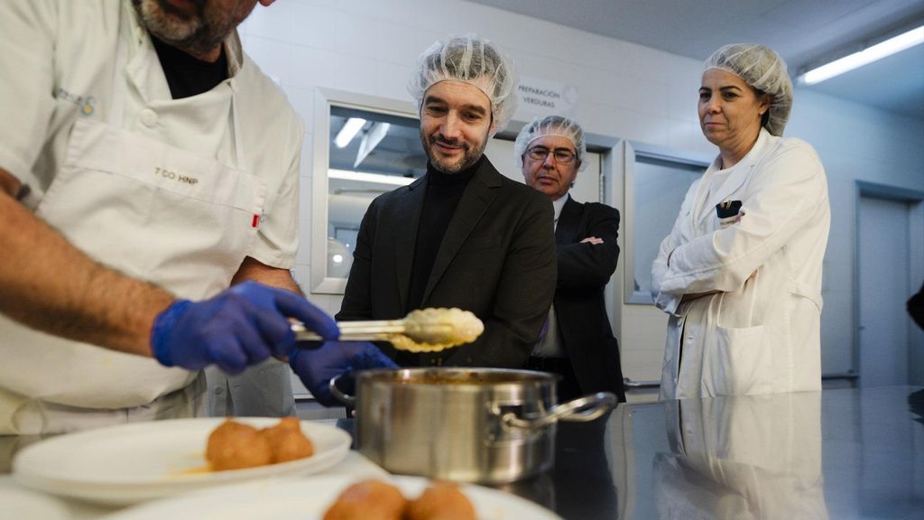 El ministro de Derechos Sociales, Consumo y Agenda 2030, Pablo Bustinduy, junto un cocinero que emplata albóndigas, durante una visita al Hospital Nacional de Parapléjicos.