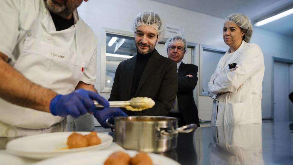 El ministro de Derechos Sociales, Consumo y Agenda 2030, Pablo Bustinduy, junto un cocinero que emplata albóndigas, durante una visita al Hospital Nacional de Parapléjicos.