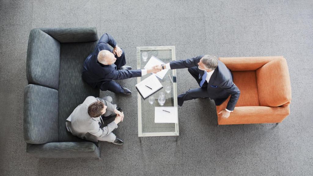 Hombres de negocios estrechándose las manos al otro lado de una mesa en oficina del lobby.