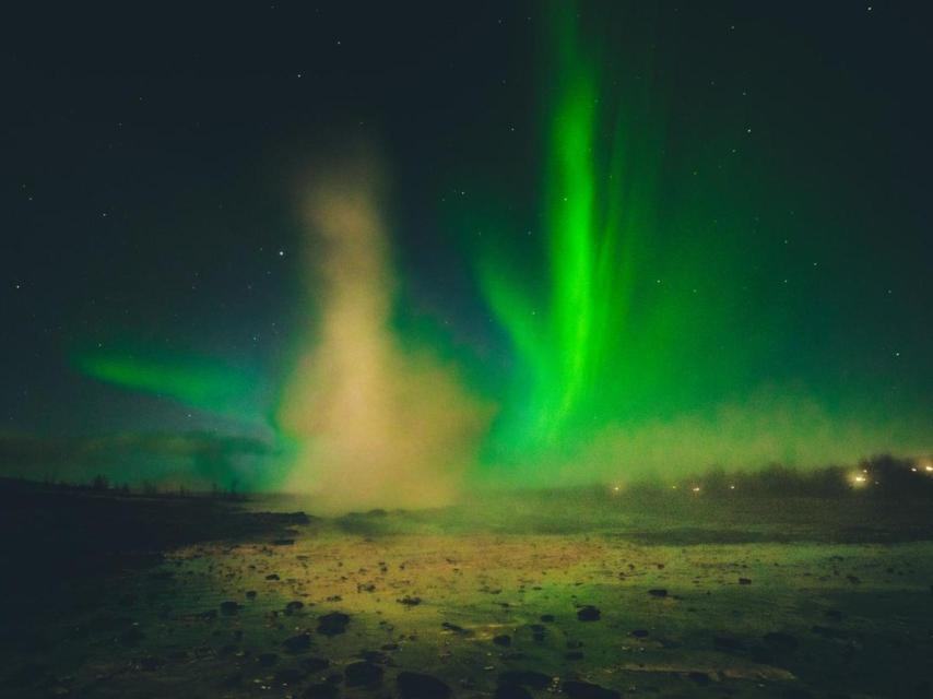 Erupción del géiser Strokkur por la noche con auroras boreales de fondo.