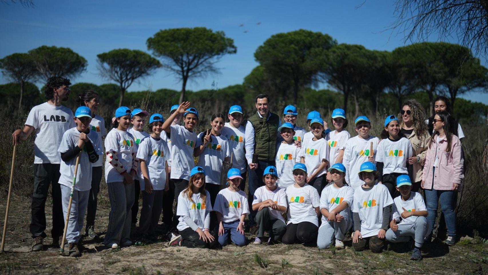 El presidente de Andalucía, Juanma Moreno, planta un árbol en Las Peñuelas junto a unos estudiantes.
