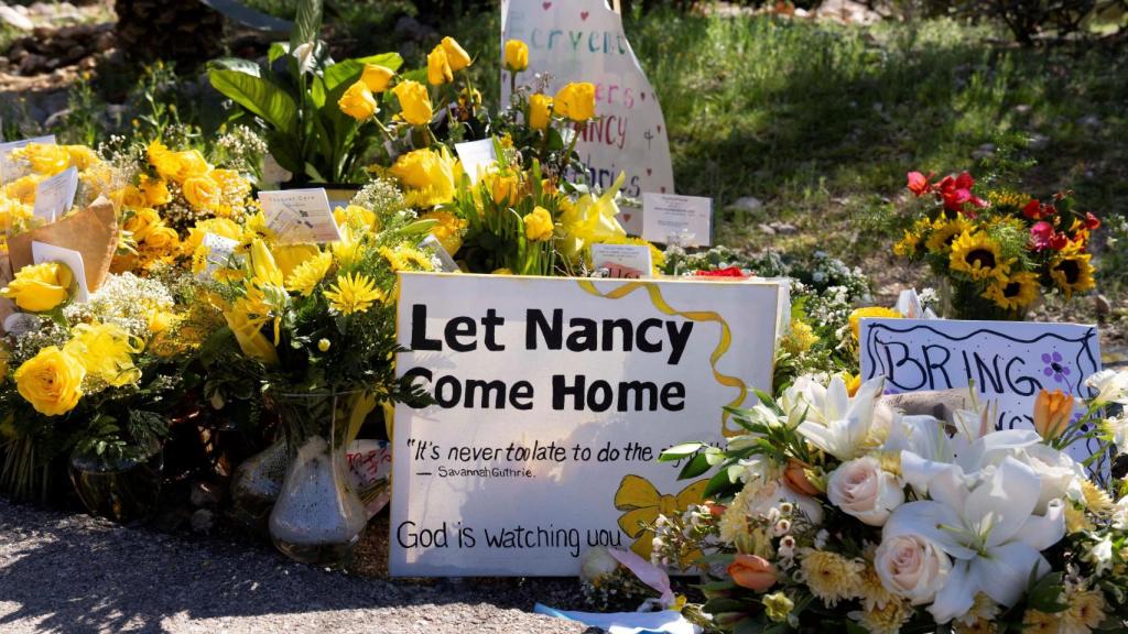 A sign says it is found among yellow flowers left at the home of Nancy Guthrie, the 84-year-old mother of American journalist and television host Savannah Guthrie.