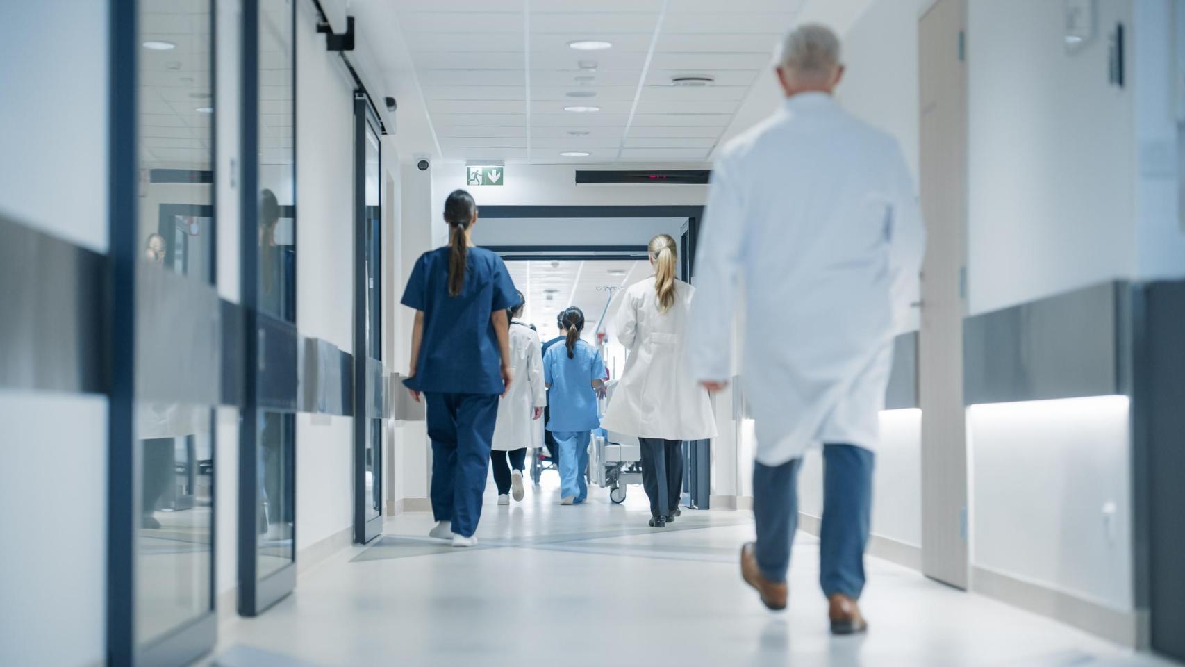 Médicas, cirujanos y funcionarios de salud caminan juntos en el pasillo de espaldas.