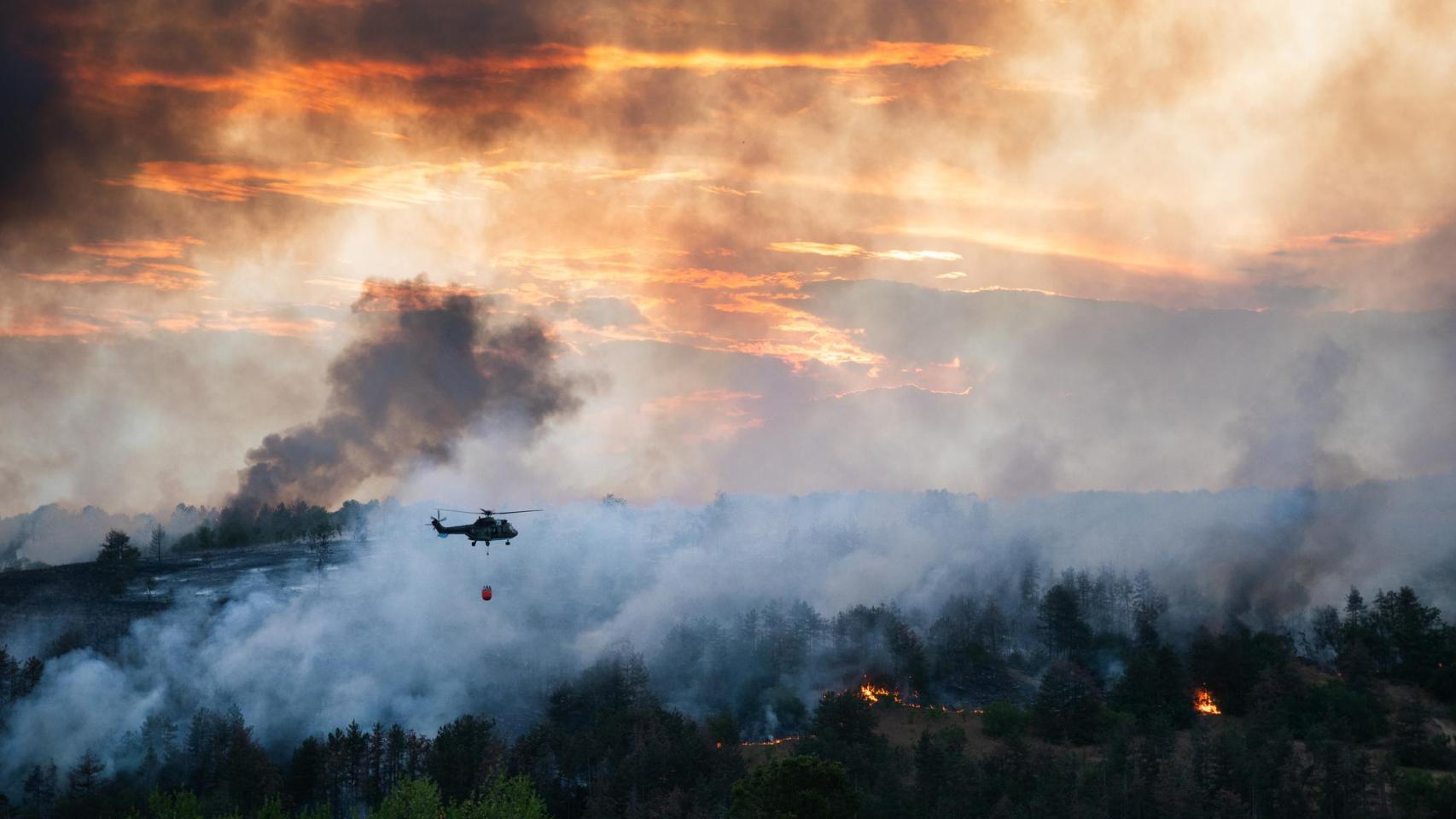 Helicóptero arrojando agua sobre un incendio forestal.