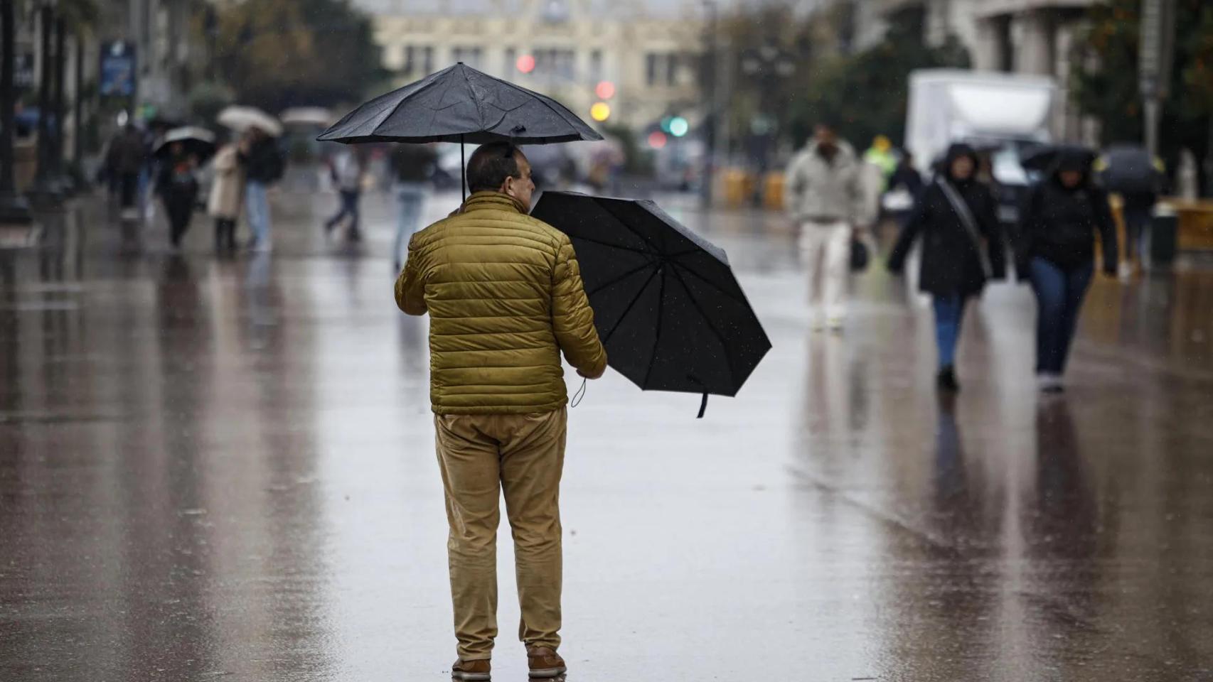 Un hombre sujeta dos paraguas bajo la lluvia en la plaza del Ayuntamiento. EFE/Biel Aliño