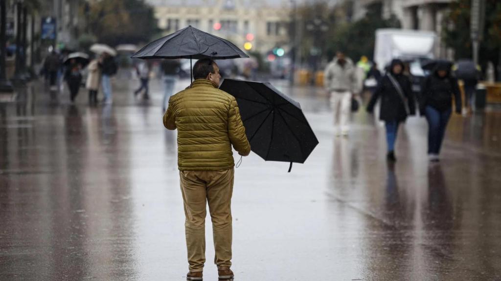 Un hombre sujeta dos paraguas bajo la lluvia en la plaza del Ayuntamiento. EFE/Biel Aliño