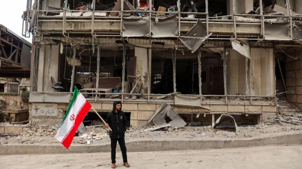 Un hombre sostiene una bandera iraní tras el ataque aéreo al hospital Gandhi Hotel en Teherán.