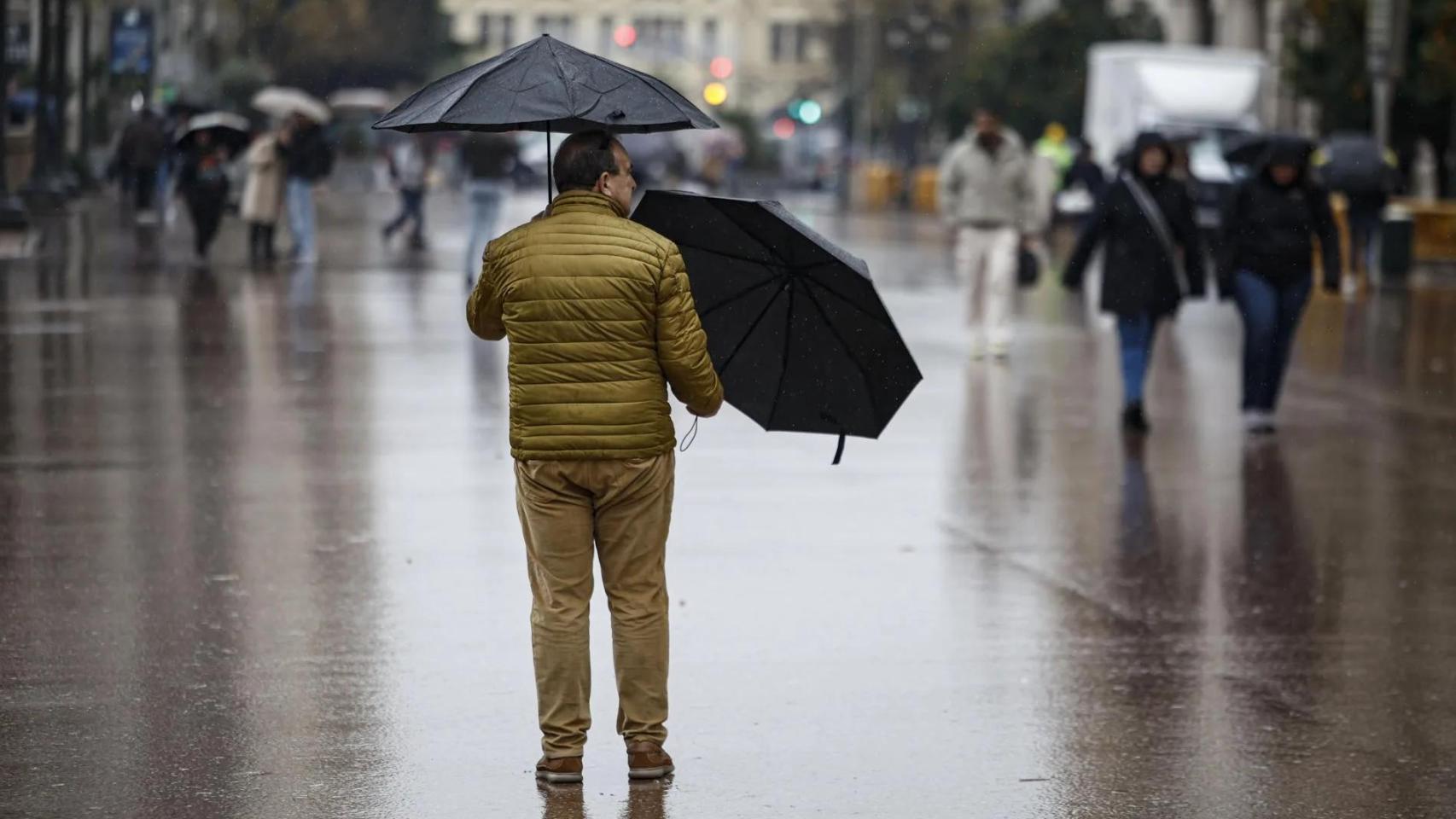 Un hombre sujeta dos paraguas bajo la lluvia en la plaza del Ayuntamiento de Valencia.