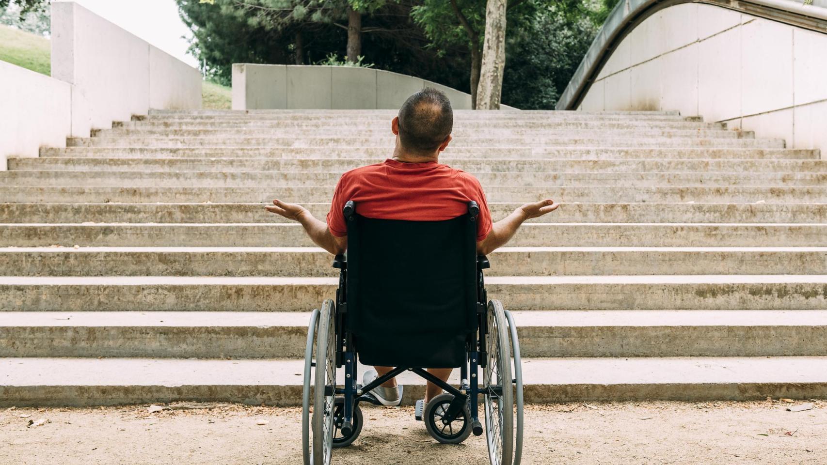 Hombre en silla de ruedas indignado frente a las escaleras.