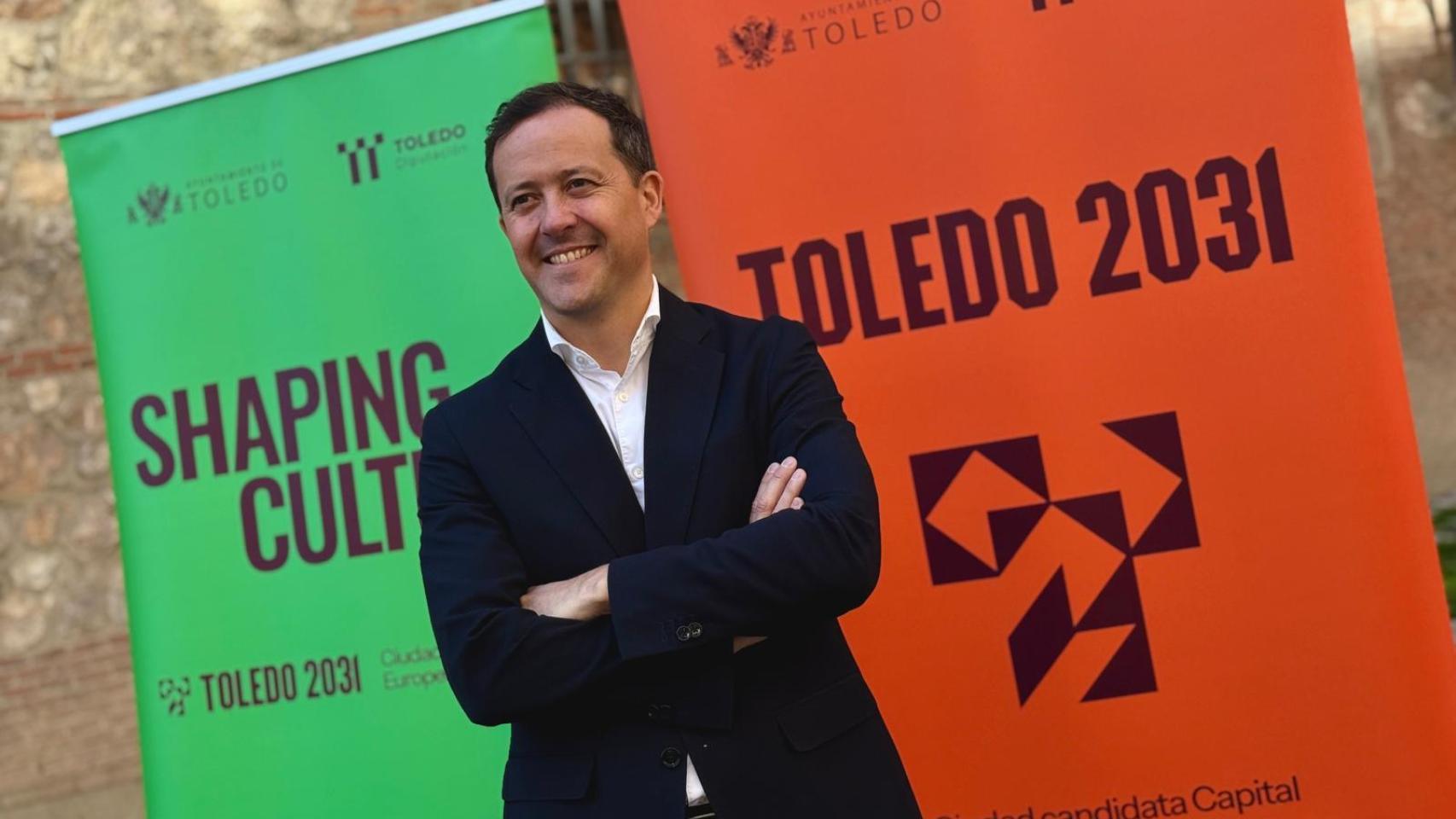 El alcalde de Toledo, Carlos Velázquez, posa satisfecho a las puertas del Ministerio de Cultura con la imagen de marca del proyecto para ser Capital Europea de la Cultura en 2031.