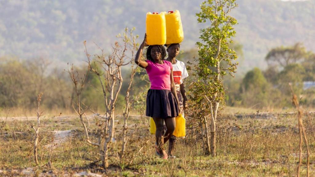 Dos niñas cargando galones de agua.