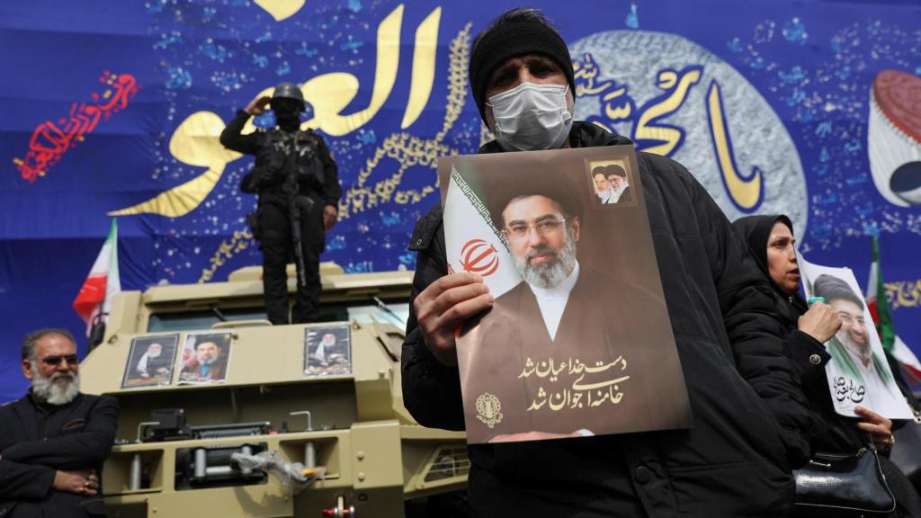 Uno hombre sostiene una imagen de Mojtaba Jamenei en Teherán ante la mirada de miembros de las fuerzas de seguridad.