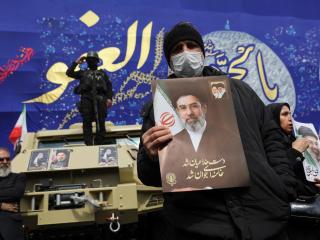 A man holds an image of Mojtaba Khamenei in Tehran as members of the security forces look on.