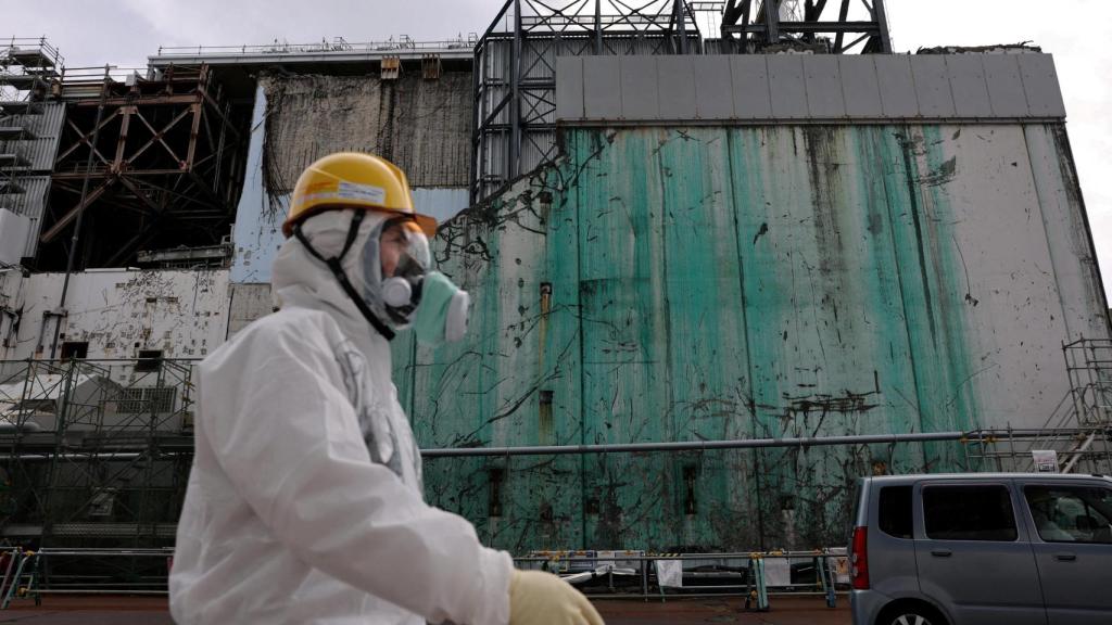 Un trabajador con un traje y una mascarilla protectora pasa junto al muro del edificio del reactor número 3 de Fukushima.