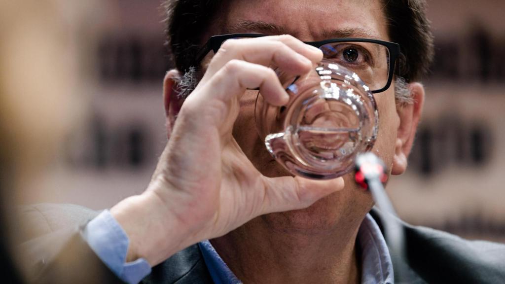 Paco Salazar se lleva el vaso a los labios en mitad de su comparecencia, como quien gana unos segundos de tregua antes de responder. Tras las gafas, la mirada fija y contenida, el gesto mínimo de quien mide cada palabra en un escenario donde todo pesa.