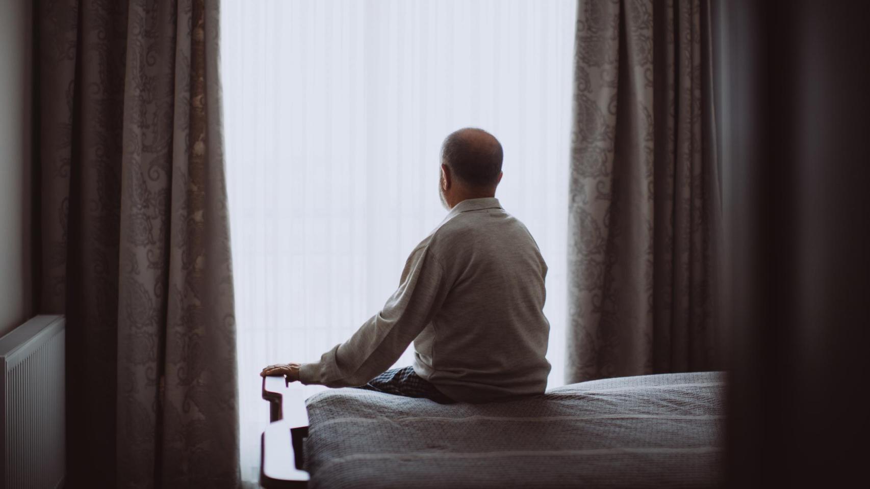 Hombre sentado en una cama mirando al horizonte.
