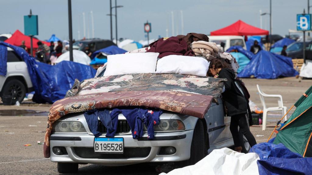 A girl looks inside a car covered with a family's belongings at a temporary camp for displaced people in Beirut