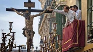 Un hombre toca un crucifijo desde un balcón de Sevilla durante la Semana Santa.