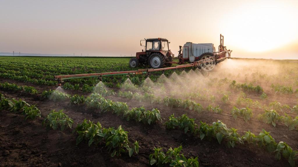 Tractor rociando pesticidas en campo vegetal con pulverizador en primavera.