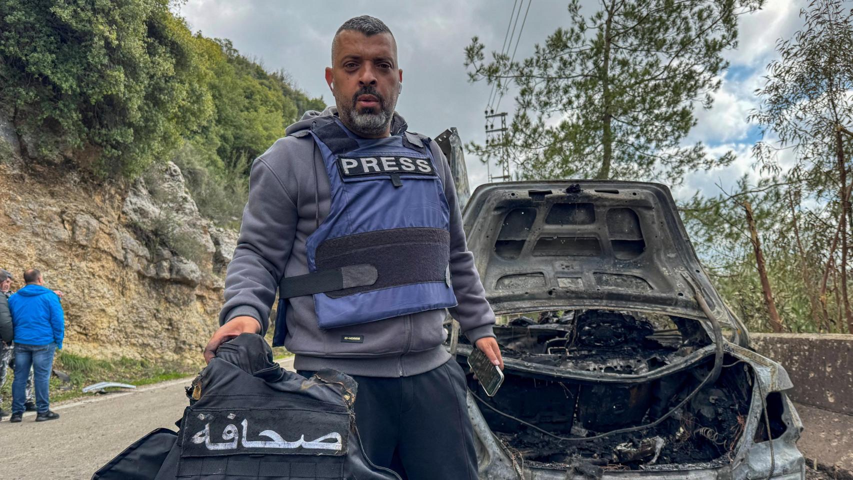 El periodista de Al Mayadeen, Jam al Al -Gharabi, sostiene un chaleco de prensa junto al automóvil destruido por un ataque israelí selectivo que mató a los periodistas libaneses