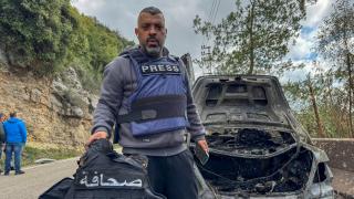 Al Mayadeen journalist Jam al Al -Gharabi holds a press vest next to the car destroyed by a targeted Israeli strike that killed the Lebanese journalists