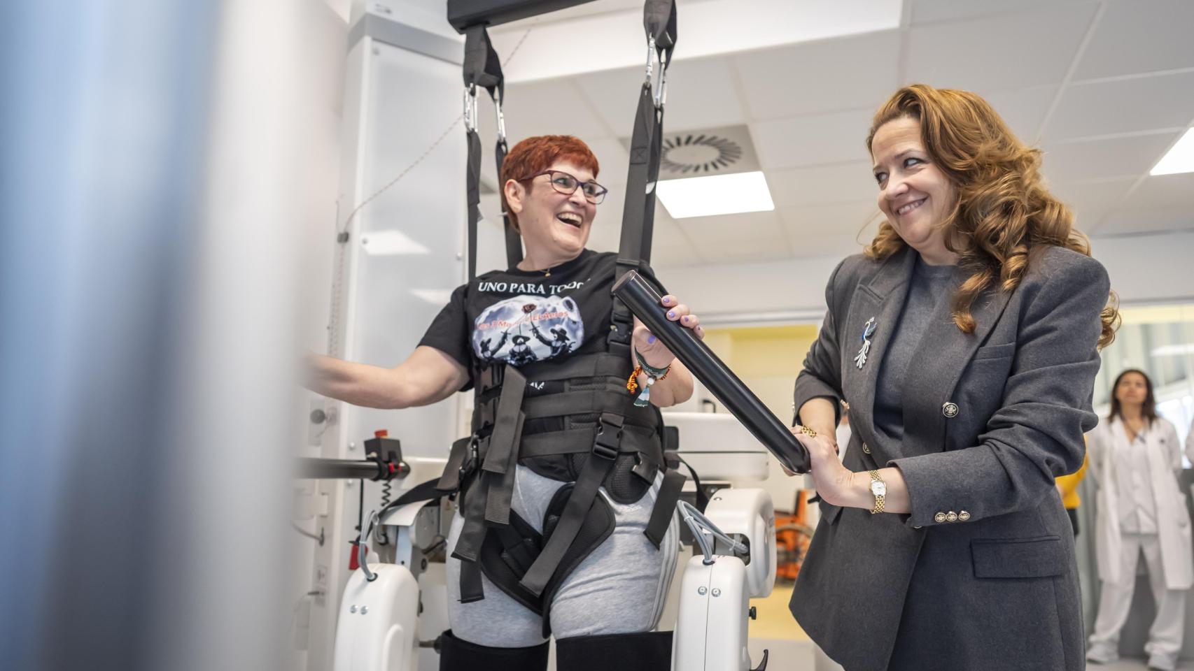 Una paciente de ELA prueba el nuevo exoesqueleto en el Hospital Isabel Zendal junto a la consejera de Sanidad de la Comunidad de Madrid, Fátima Matute.