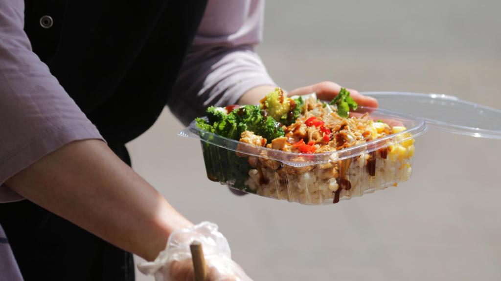 Un camarero introduce las sobras de una comida en un envase de plástico.