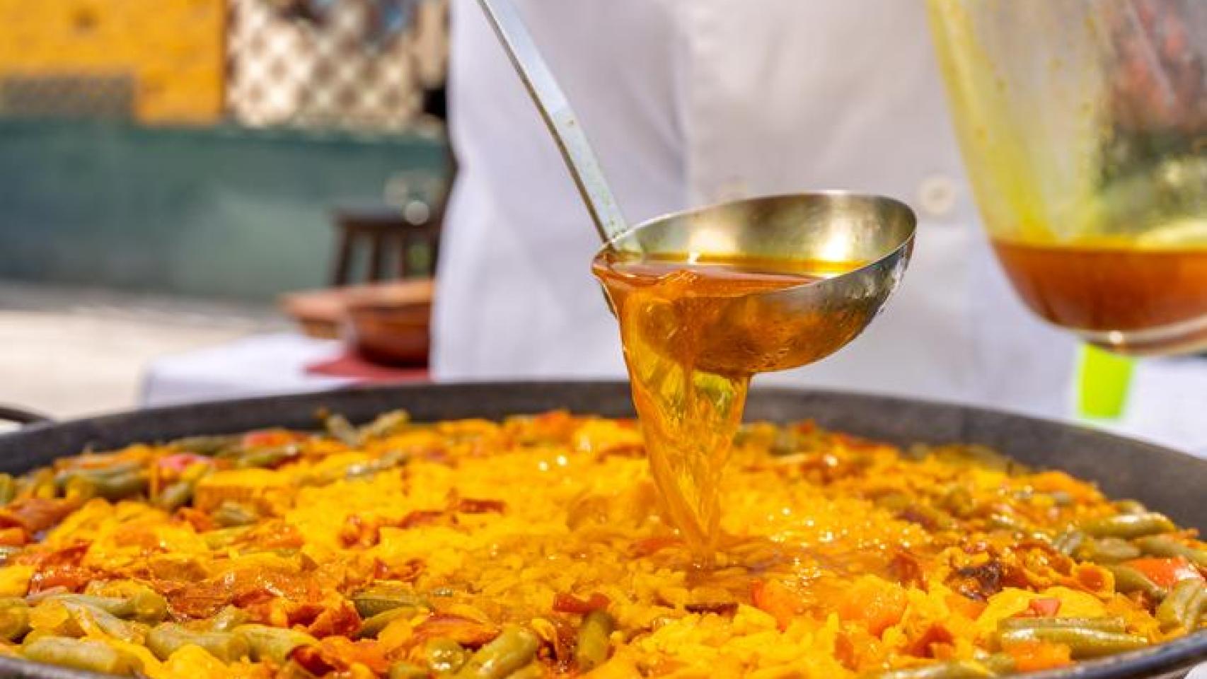 Cocinero añadiendo caldo a la paella.