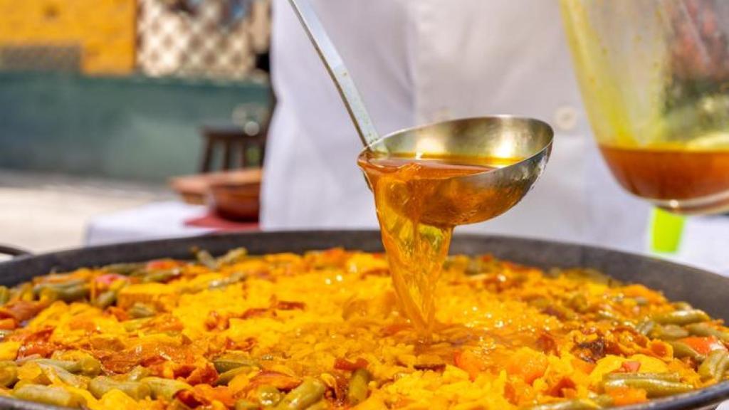 Cocinero añadiendo caldo a la paella.