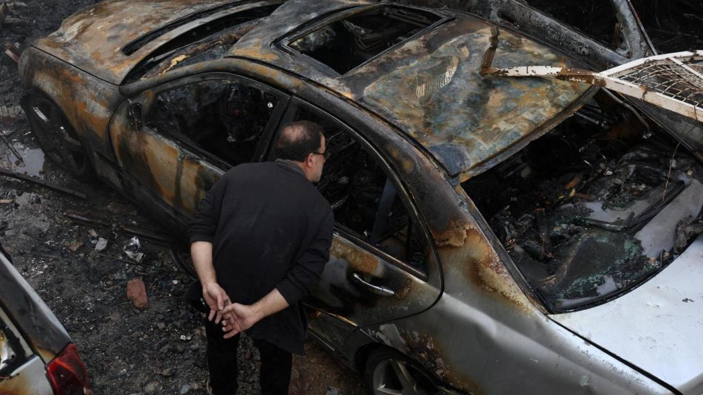 A Beirut resident inspects a burned-out car.