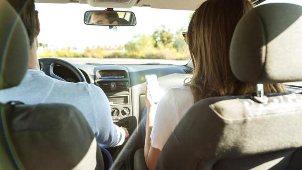 Pareja que viaja dentro del coche mirando el teléfono móvil.