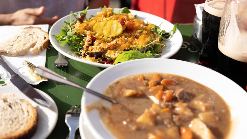 Primer plano de dos platos de comida con pan y cerveza Guinness en una mesa en una terraza exterior en Dublín.