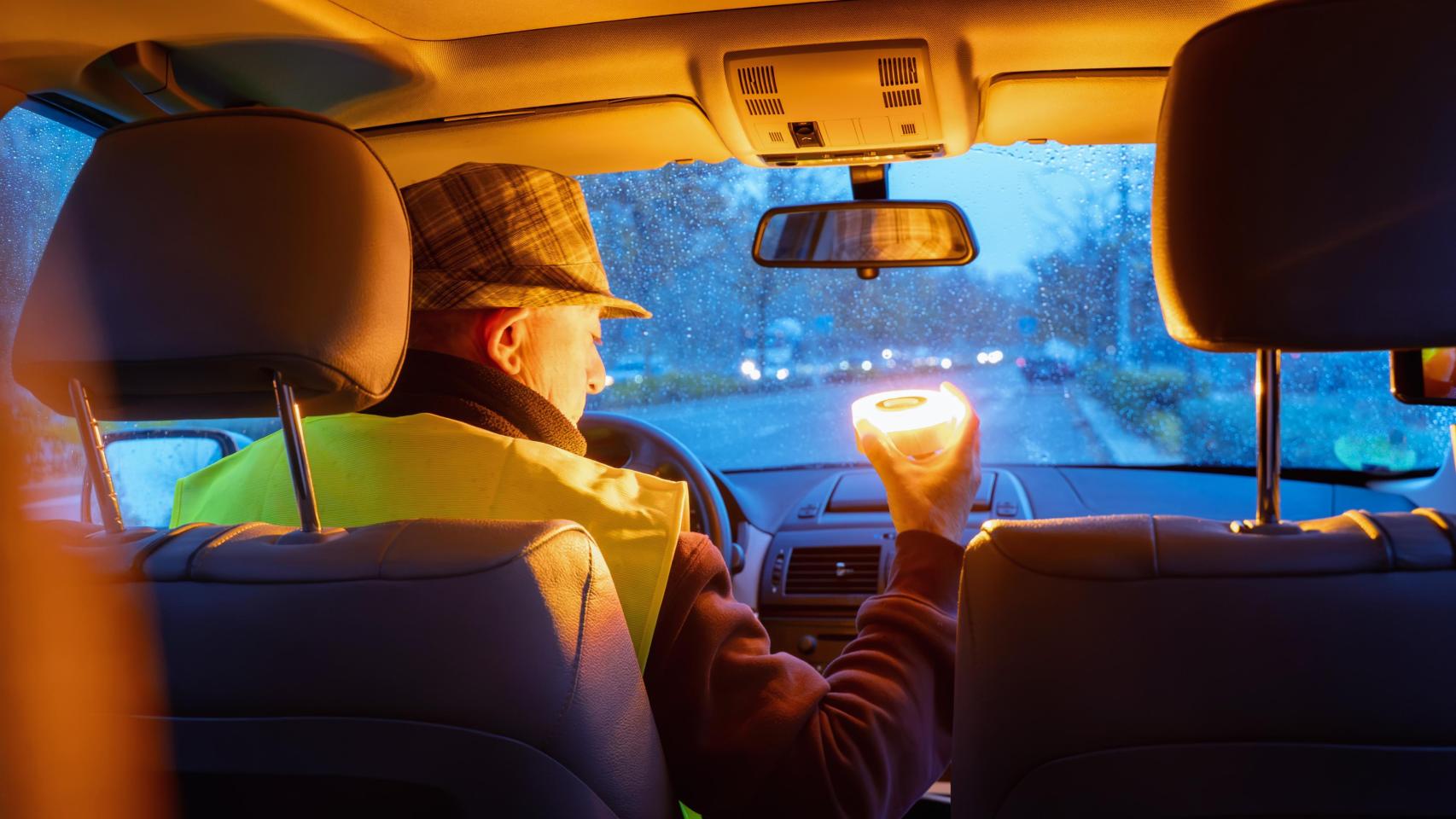 Conductor sosteniendo una baliza de emergencia V16 en el coche durante una avería en la carretera.
