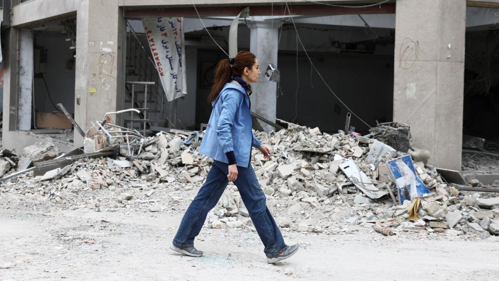 Una mujer camina frente a un edificio en ruinas debido al conflicto.