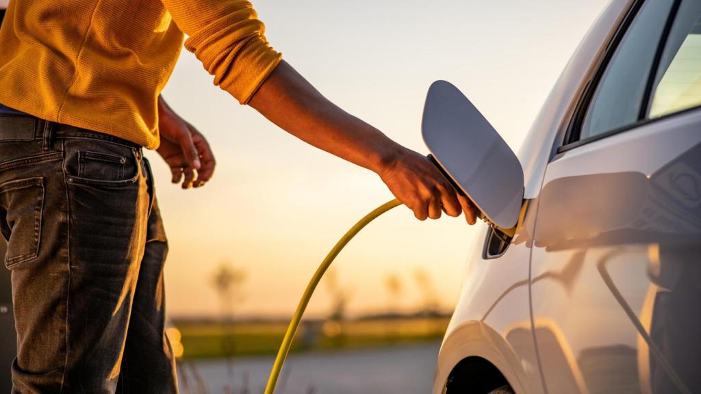 Hombre insertando enchufe en la toma de carga del coche eléctrico.