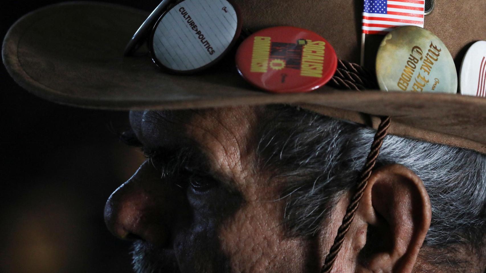 Un hombre engalana su sombrero vaquero con una bandera estadounidense.